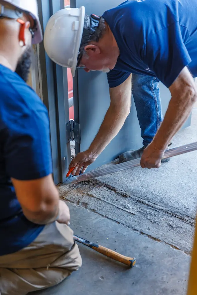 two construction workers with hard hats repairinf a door frame