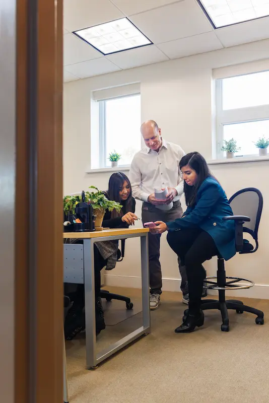 two women and one man sharing documents in a small bright office