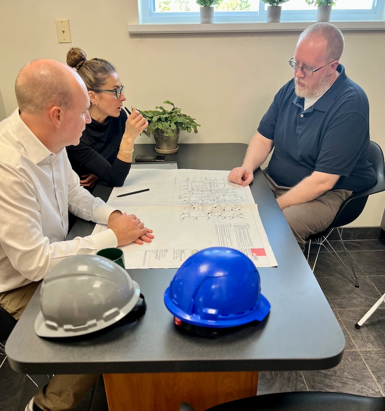 two men and one women discussing plans around a table