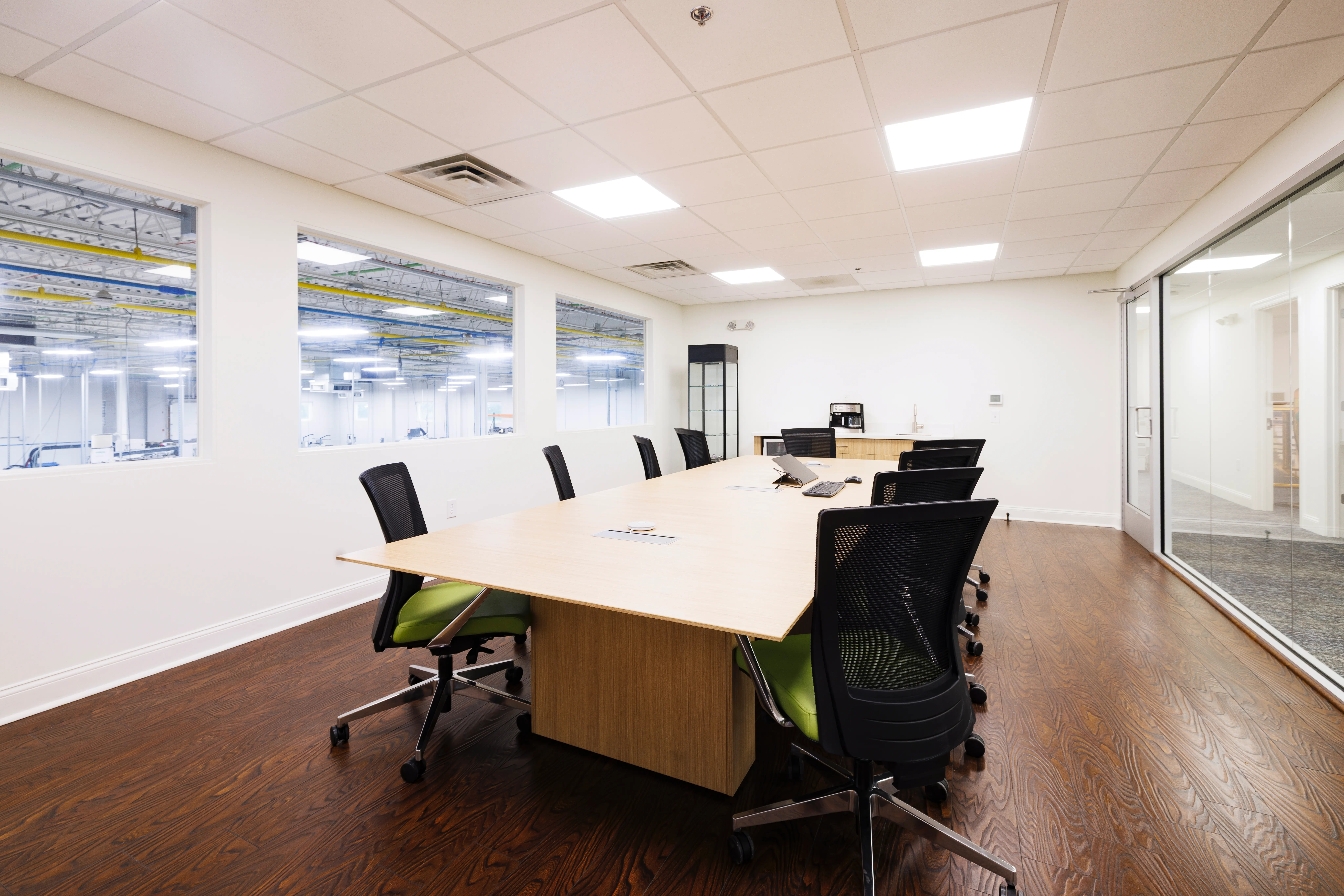 bright conference room with long table surrounded by black chairs overlooking a production area