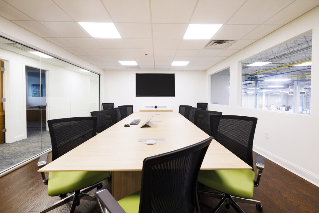 bright board room with large table overlooking manufacturing area on one side and large glass doors on the other