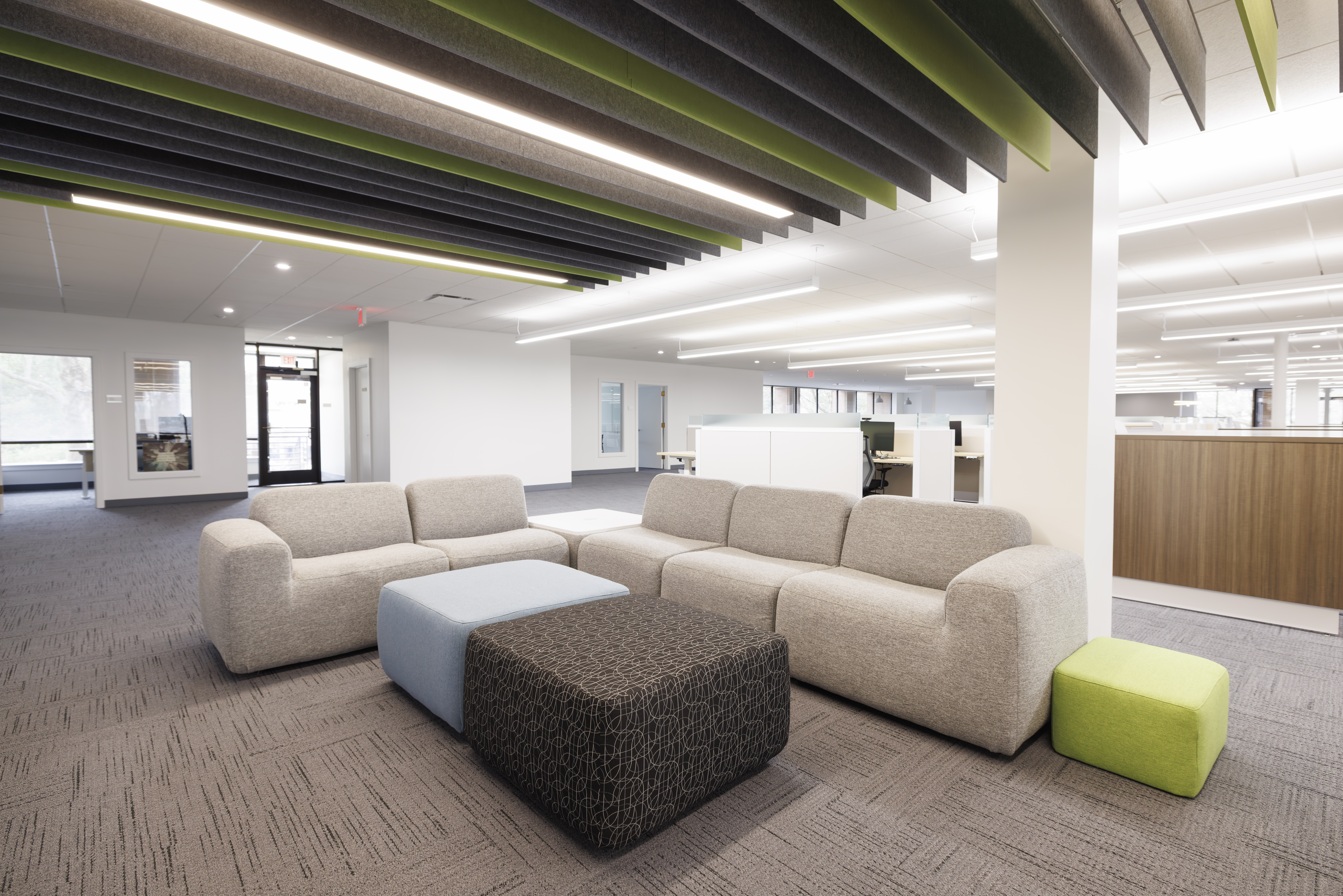 Modern office seating area with gray couches, yellow pillows, and a wooden table under bright LED lighting.