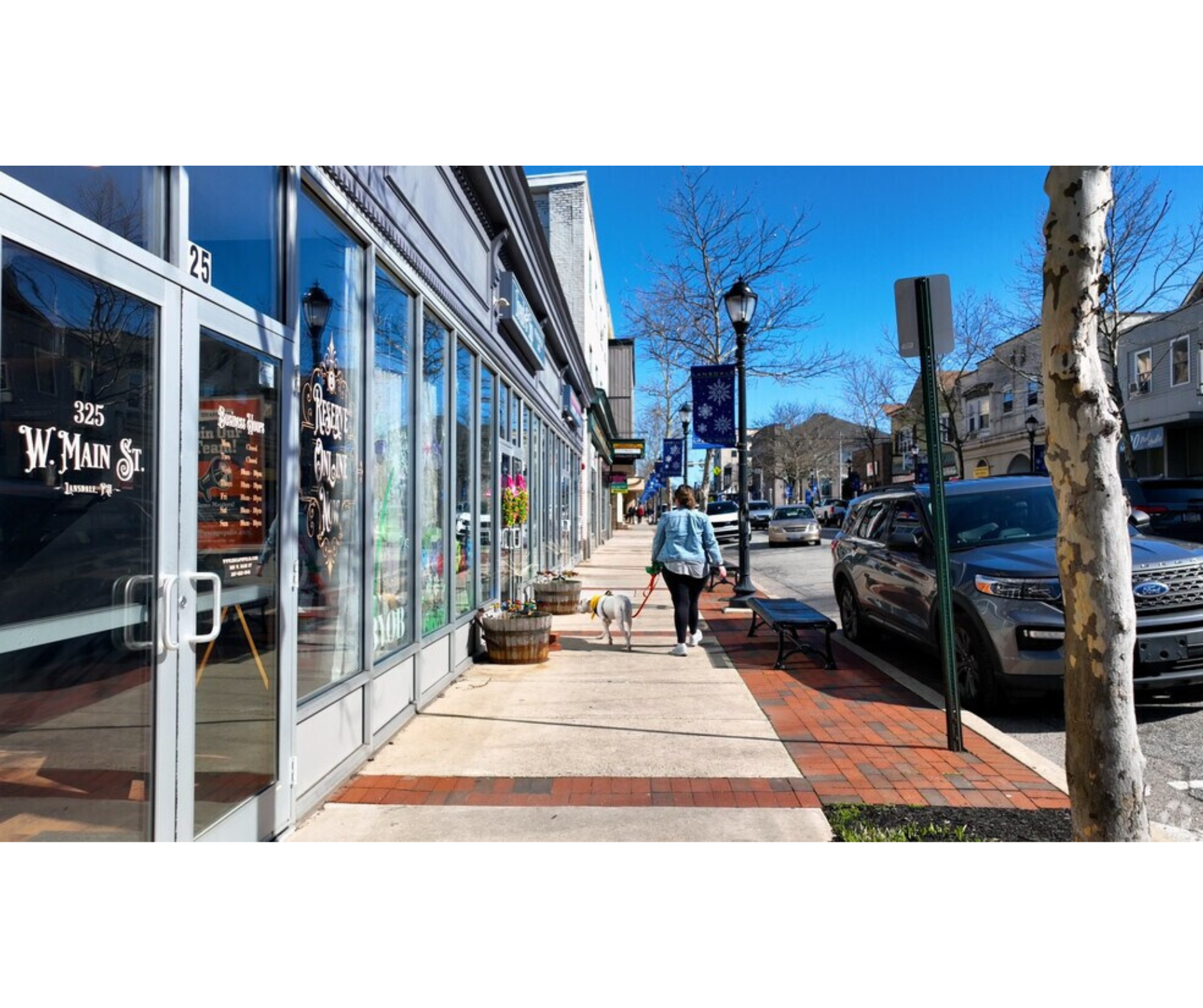 retail stores shown left with a women and dog walking on sidewalk in front of store on a sunny day
