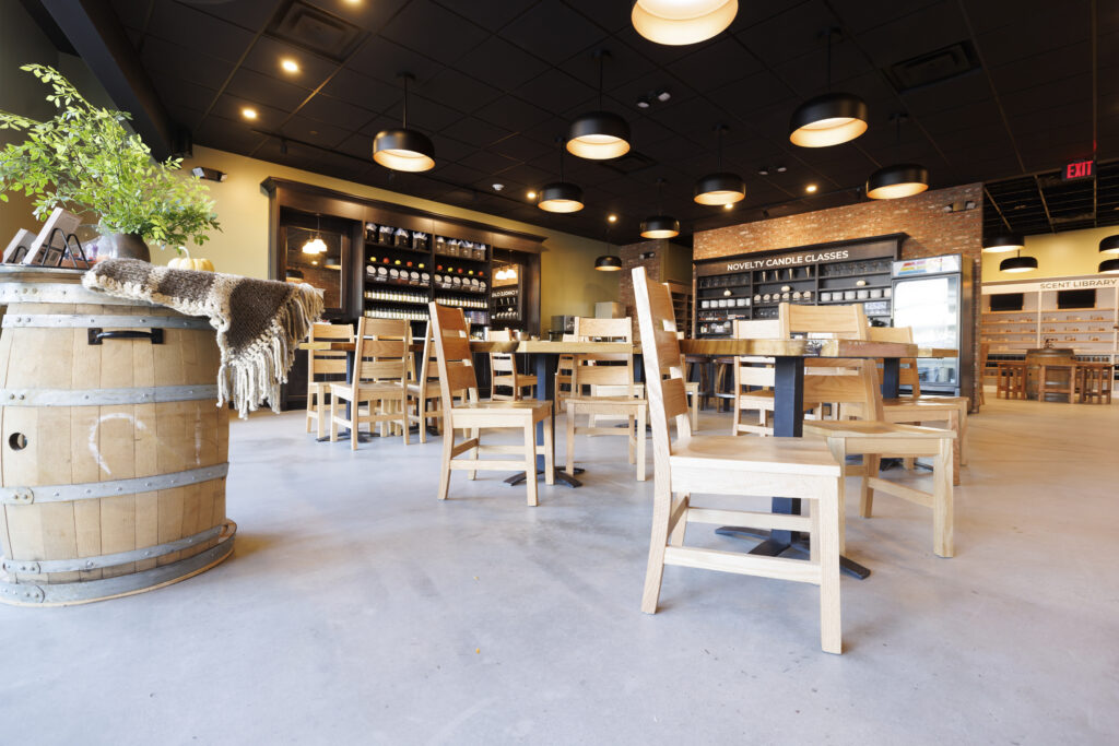 wooden tables and chairs in the foreground and wooden shelves of candles in the background with black ceiling and hanging black lights